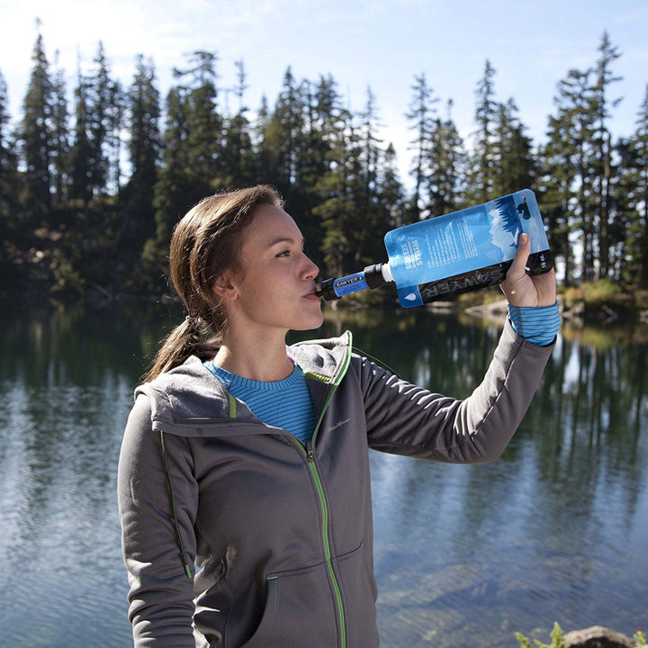 woman drinking from sawyer filter in front of lake